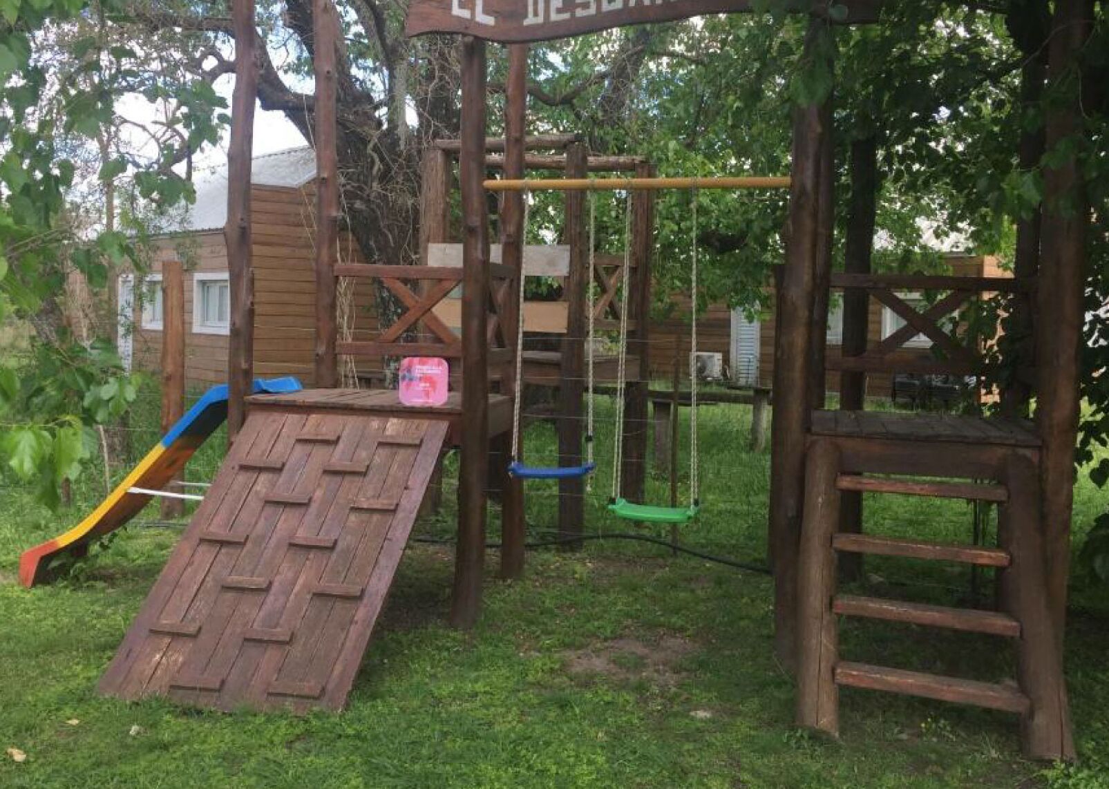 A wooden play structure with a slide, swings, and a climbing ladder.
