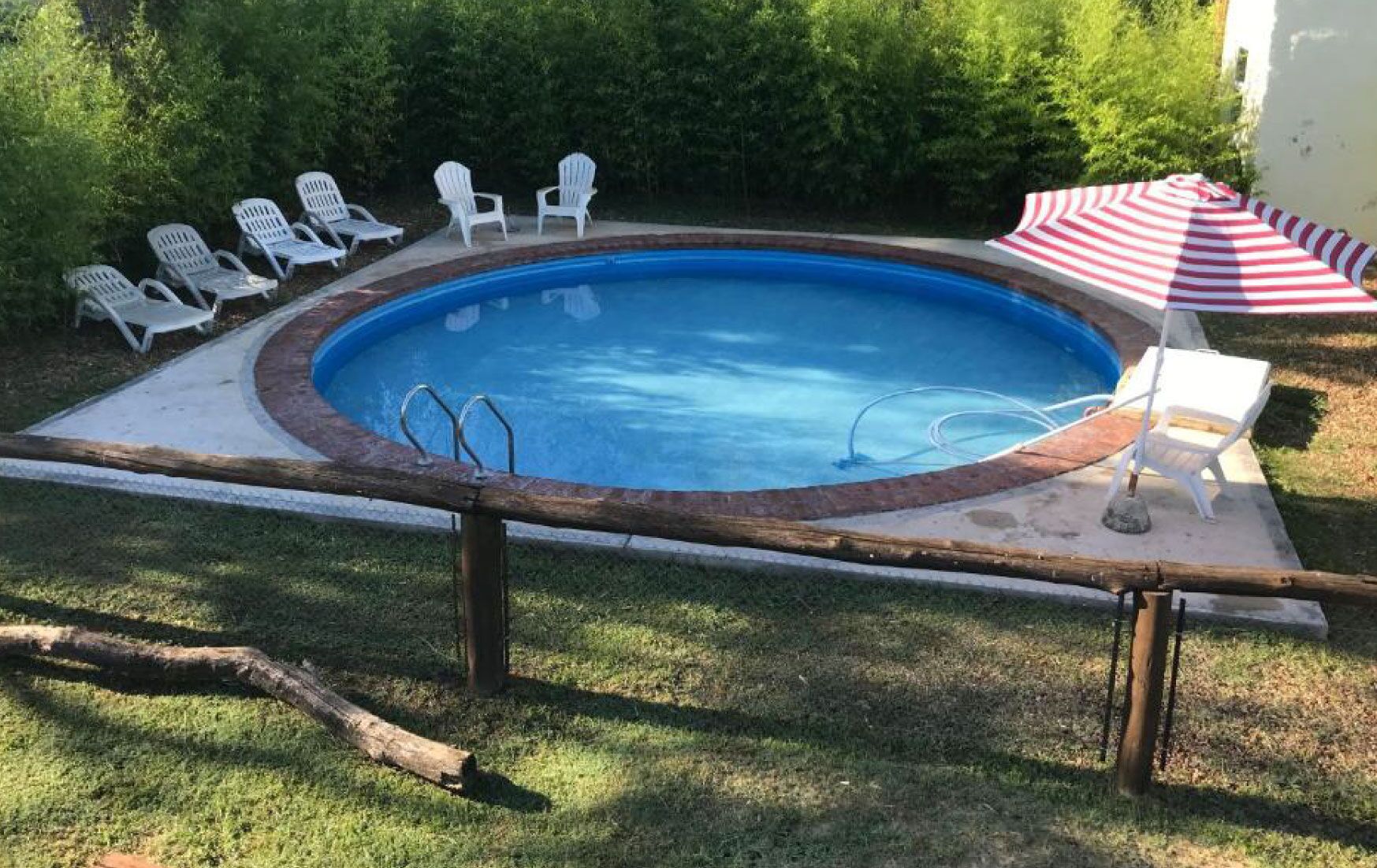 Een zwembad met een houten terras, omringd door witte ligbedden en een gestreepte parasol.