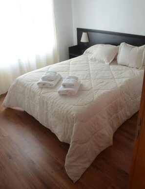 A neatly made bed with a quilted white comforter and two folded white towels.