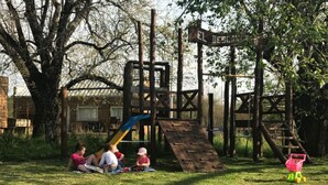 A playground with a slide and climbing structures, surrounded by trees and grass. - El Descanso (Colon)
