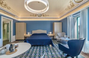 Une chambre d’hôtel dotée d’un grand lit, d’un coin salon avec un fauteuil et une table, d’un petit bureau et offrant une vue sur l’extérieur.