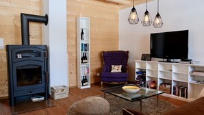 Un salon chaleureux avec un poêle à bois, un fauteuil confortable de couleur violette, une table basse en verre et une bibliothèque remplie de livres et de bouteilles.