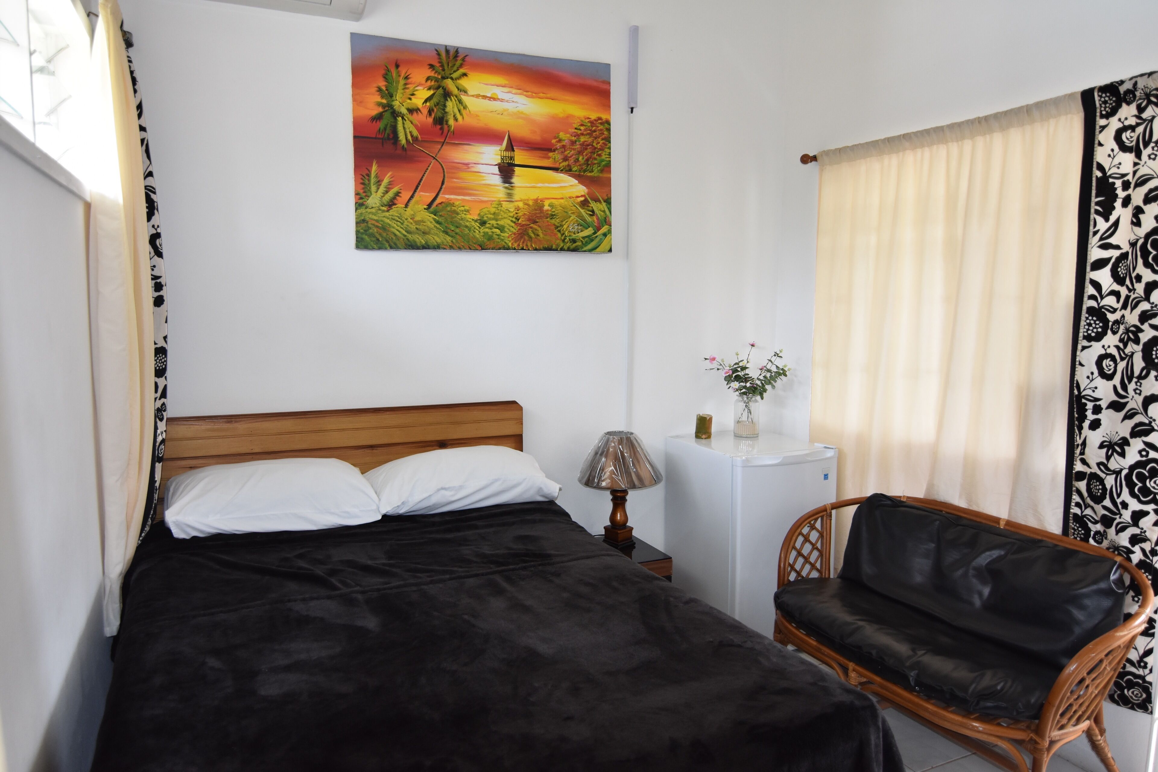 Ein Schlafzimmer mit Bett, Nachttisch, Lampe, Sessel, Gemälde und Vorhängen.