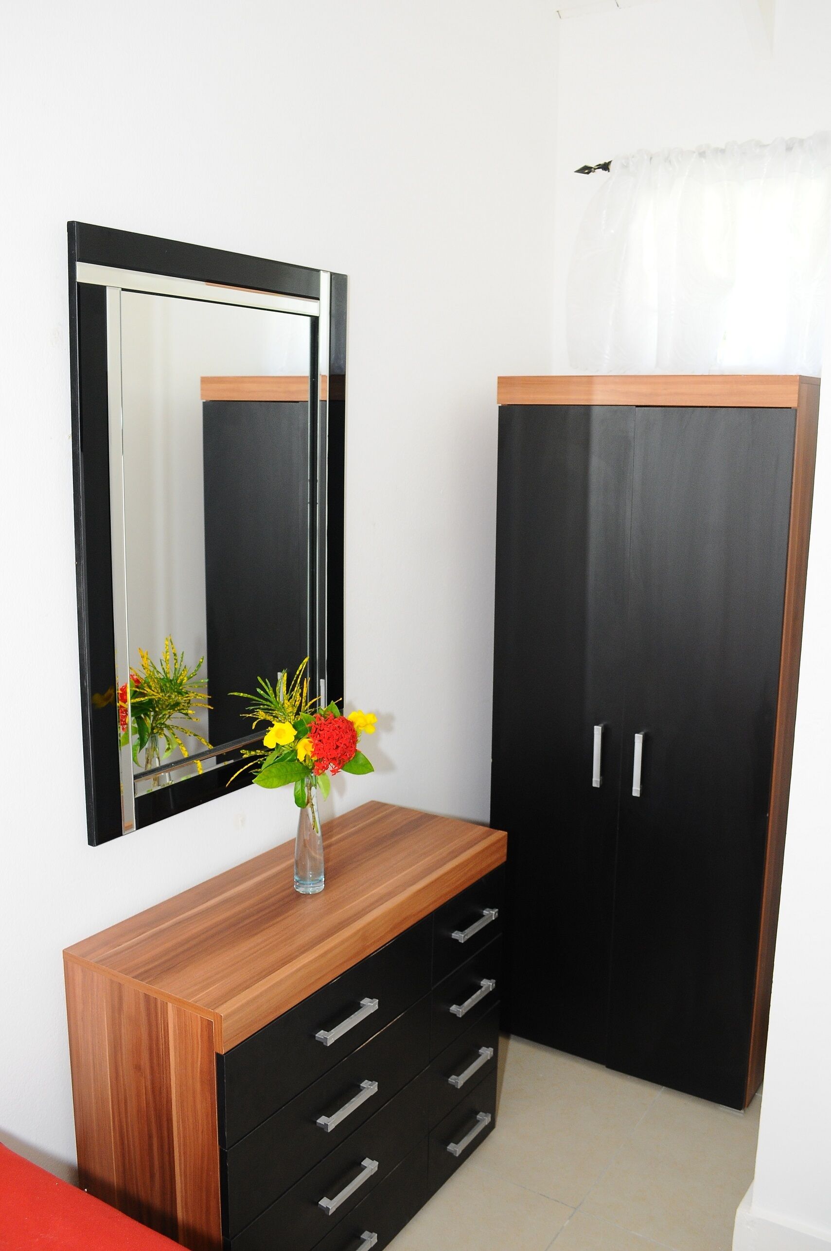 Ein Zimmer mit einem Holzschrank, einem schwarzen Kleiderschrank und einem Spiegel an der Wand.