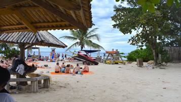 Una playa con gente tomando el sol y un barco al fondo.
