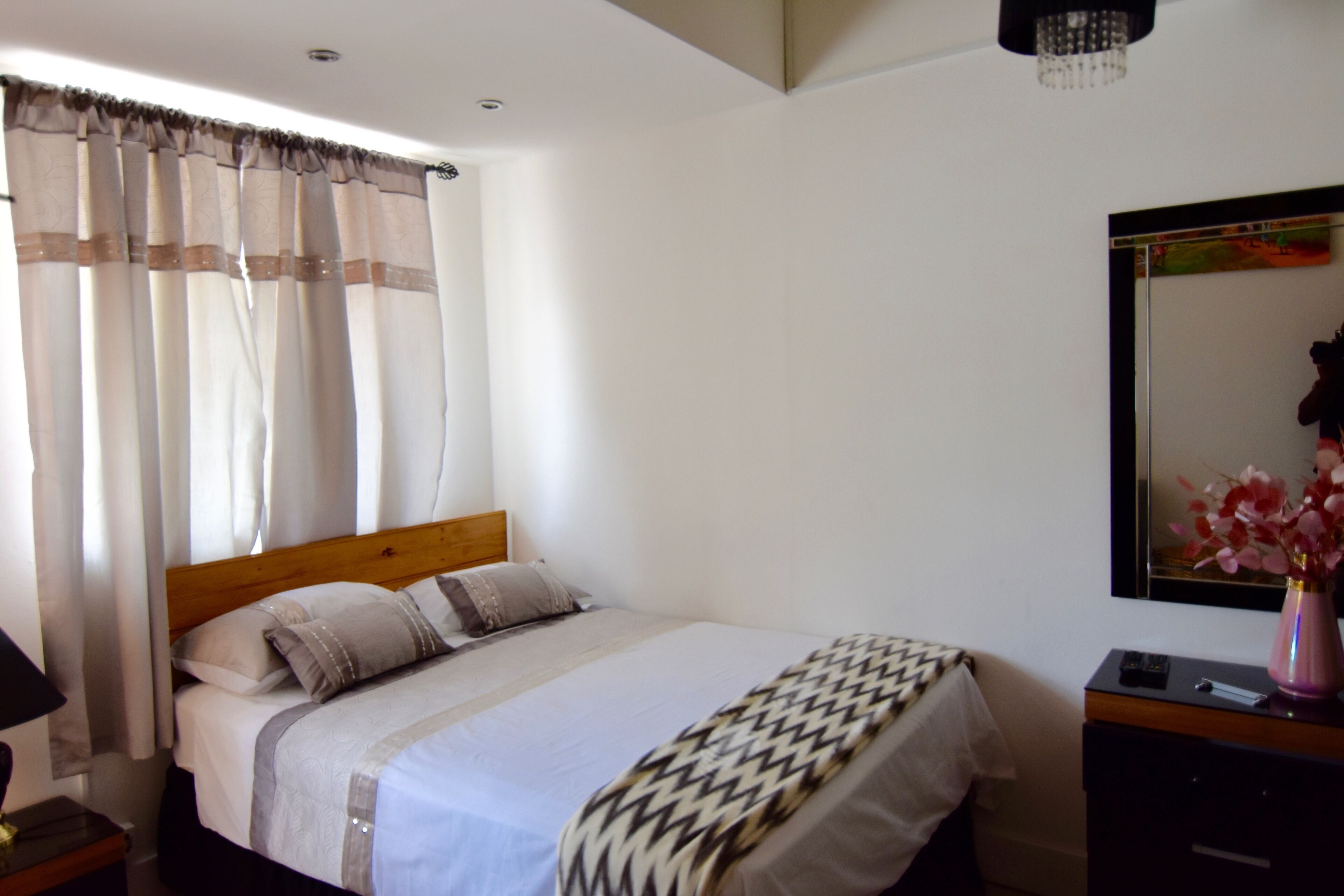 A neatly made bed with a wooden headboard, a bedside table with a lamp, and a mirror on the wall.