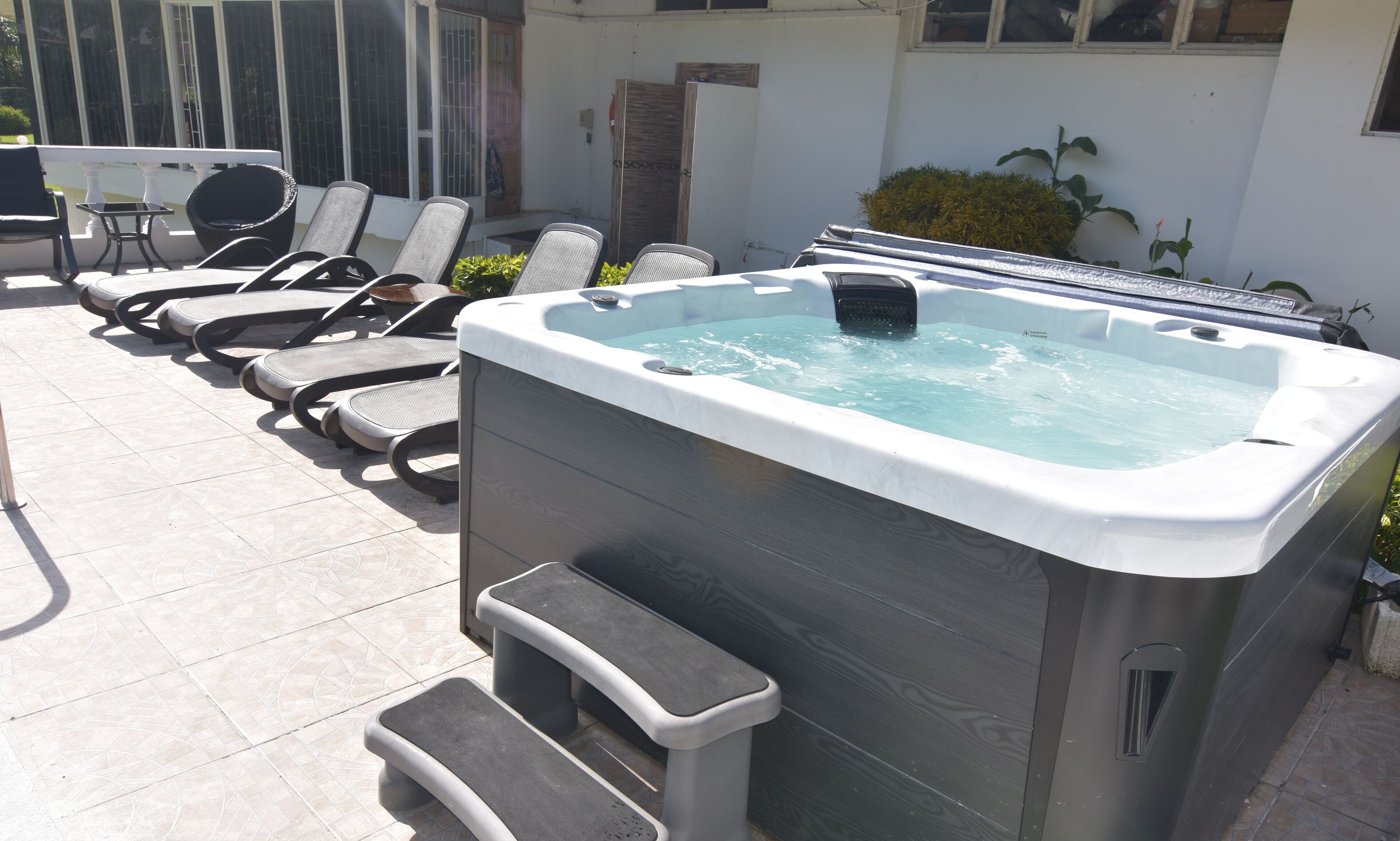 Een hottub met een houten buitenkant en een ingebouwde zitplaats, omringd door lounge stoelen en een bijzettafeltje.