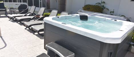 A hot tub with a wooden exterior and a built-in seat, surrounded by lounge chairs and a small table.