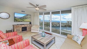 A spacious living room with a large TV, a ceiling fan, and a view of the ocean through large sliding doors. - Perfect family retreat! Large deck for relaxing the sun! (Destin)