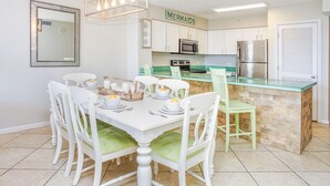 A modern kitchen with white cabinetry, a green island, and a dining area with white chairs and a table set for four. - Perfect family retreat! Large deck for relaxing the sun! (Destin)