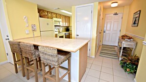 A kitchen with a central island, bar stools, a microwave, a refrigerator, and a door leading to another room. - Relax and Catch a couple fish! Drop all your worries it's vacation time. 🕮🏖️ (Gulf Shores)