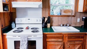 A kitchen with wooden cabinets, a white stove, a sink, and a window with a view of trees.