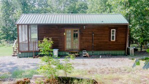 A wooden cabin with a metal roof, a front porch, and a small deck.