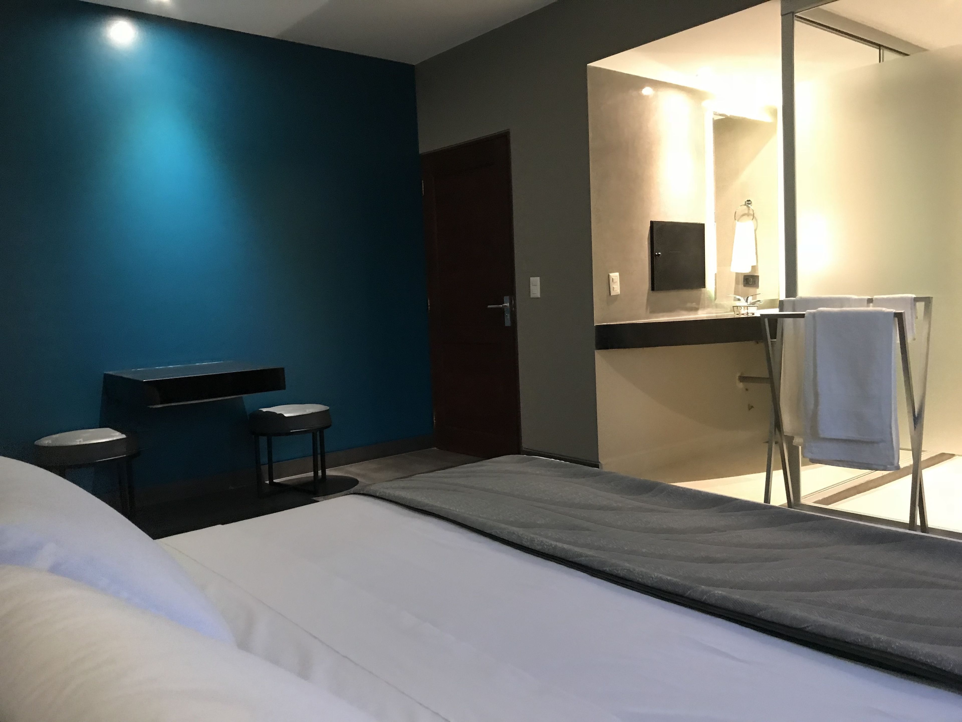 A hotel room with a bed, a small seating area, a bathroom with a mirror, and a towel rack.