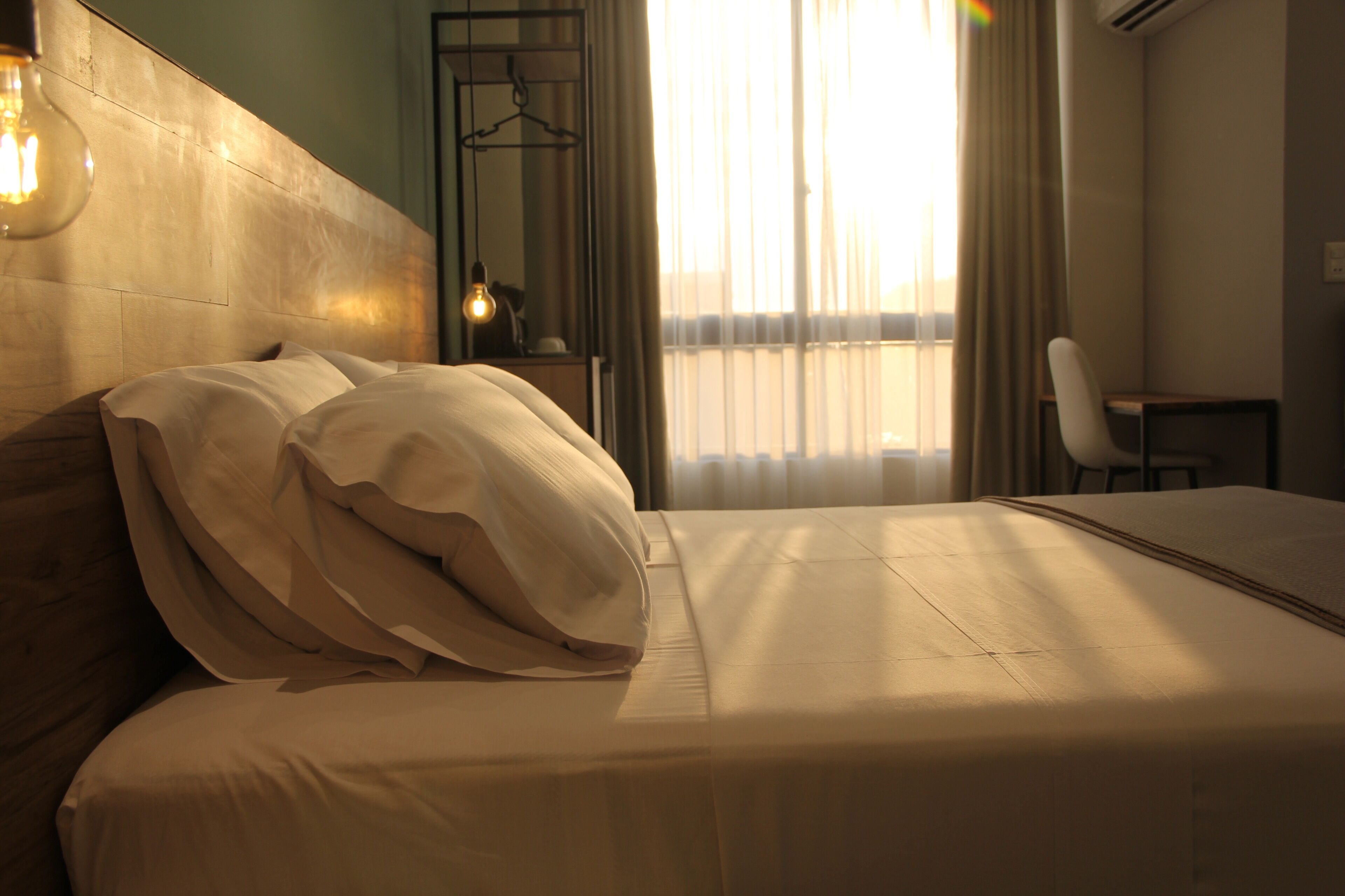 Quarto de hotel com cama, uma cadeira, mesa de cabeceira e janela com cortinas.