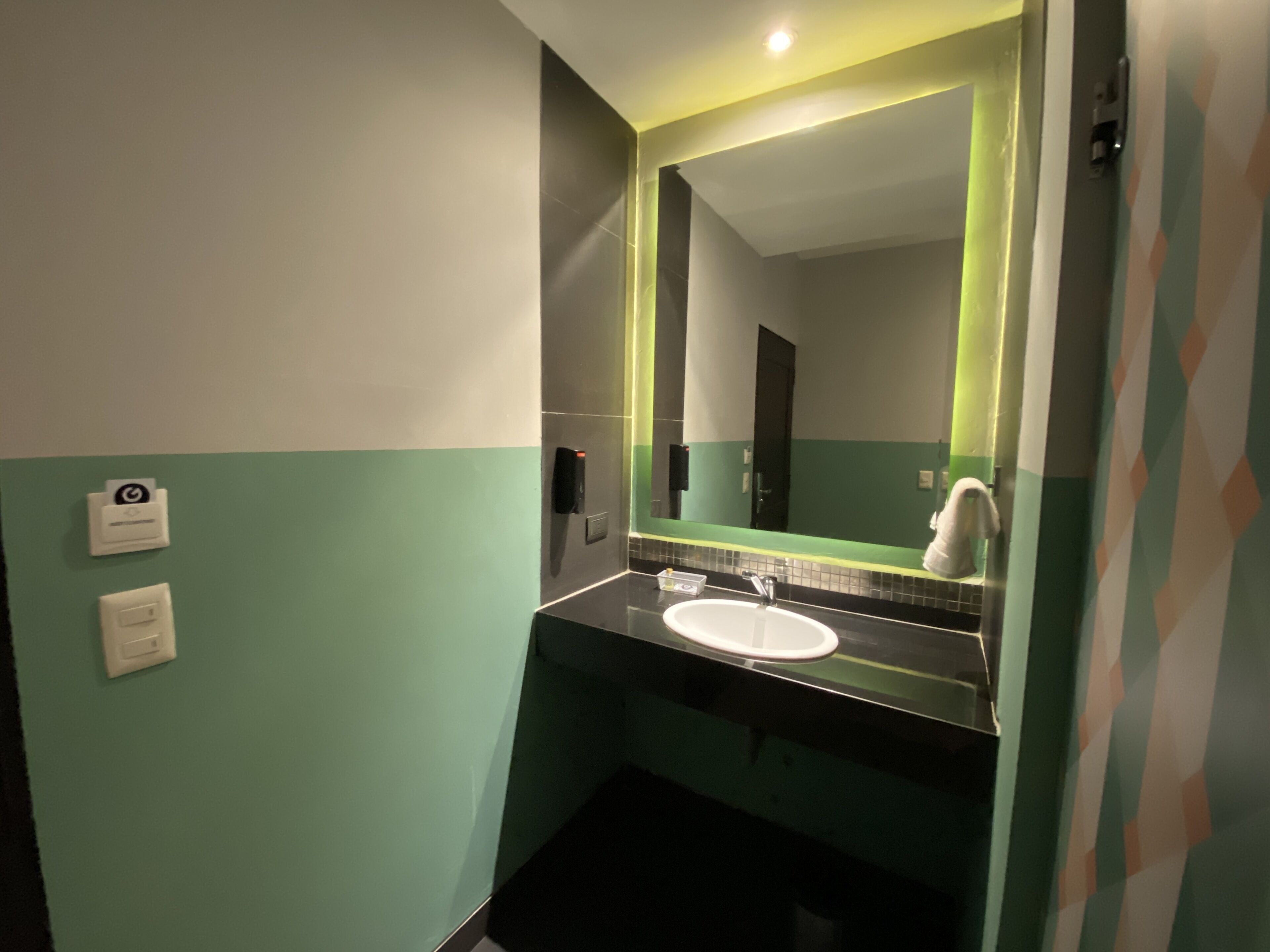 Une salle de bain avec un lavabo blanc, des murs verts et un miroir doté d’un cadre vert.