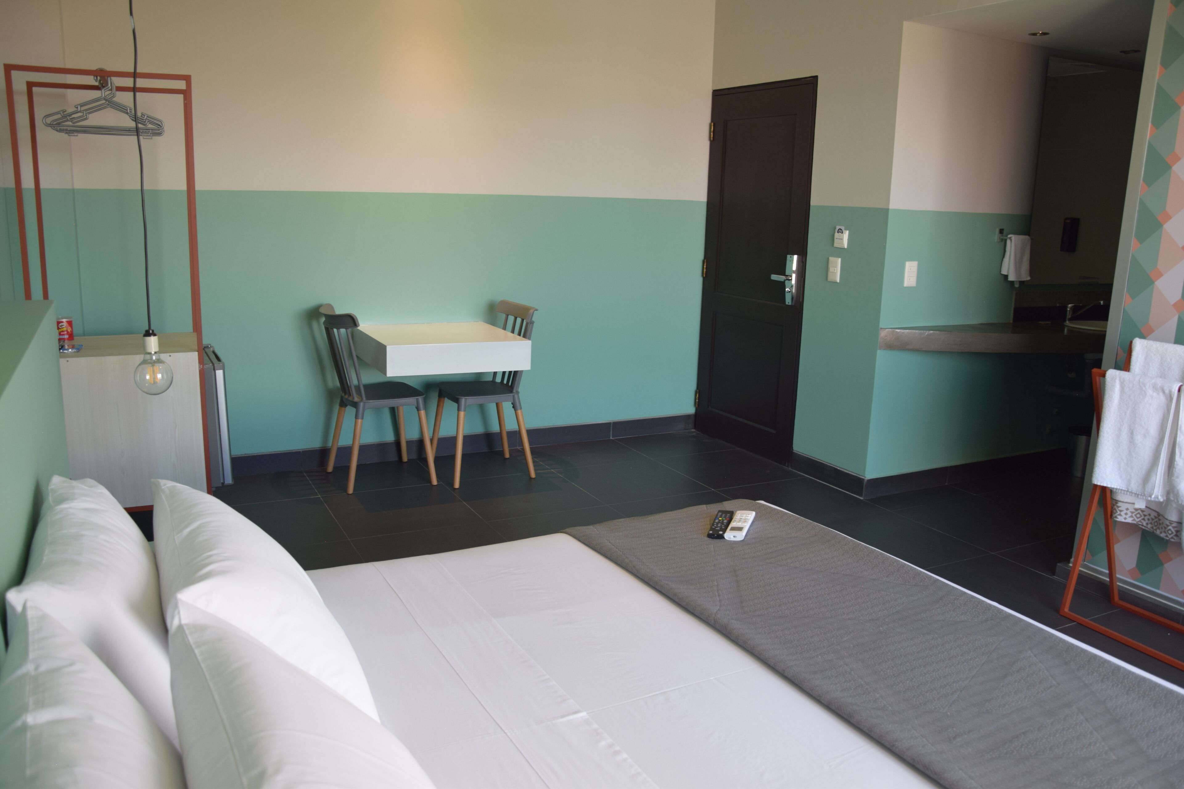 Ein Hotelzimmer mit Bett, Schreibtisch und Stuhl. Auf dem Bett liegt eine Fernbedienung.