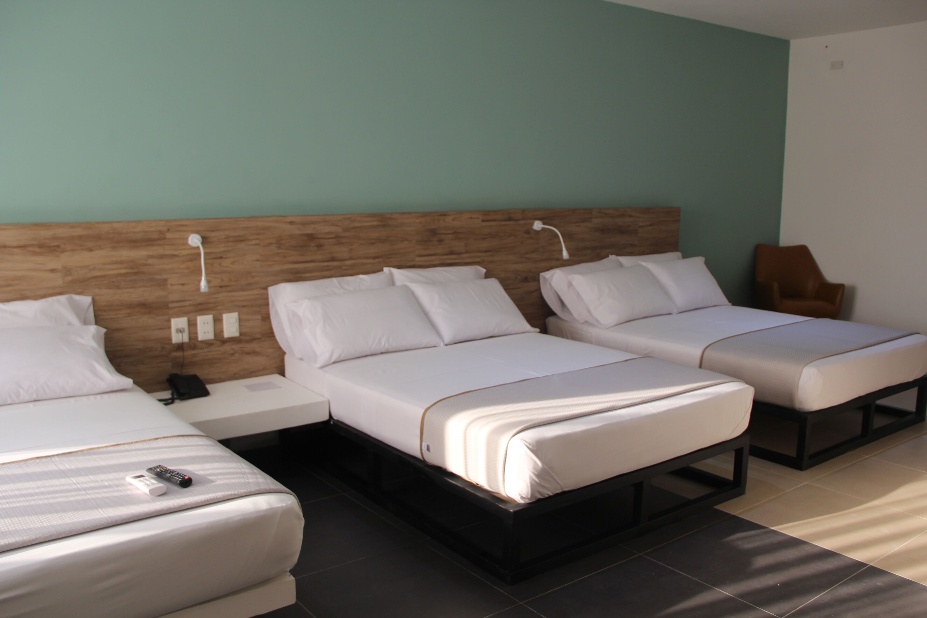 A hotel room with two single beds, a wooden headboard, a bedside table with a phone, and a brown chair.