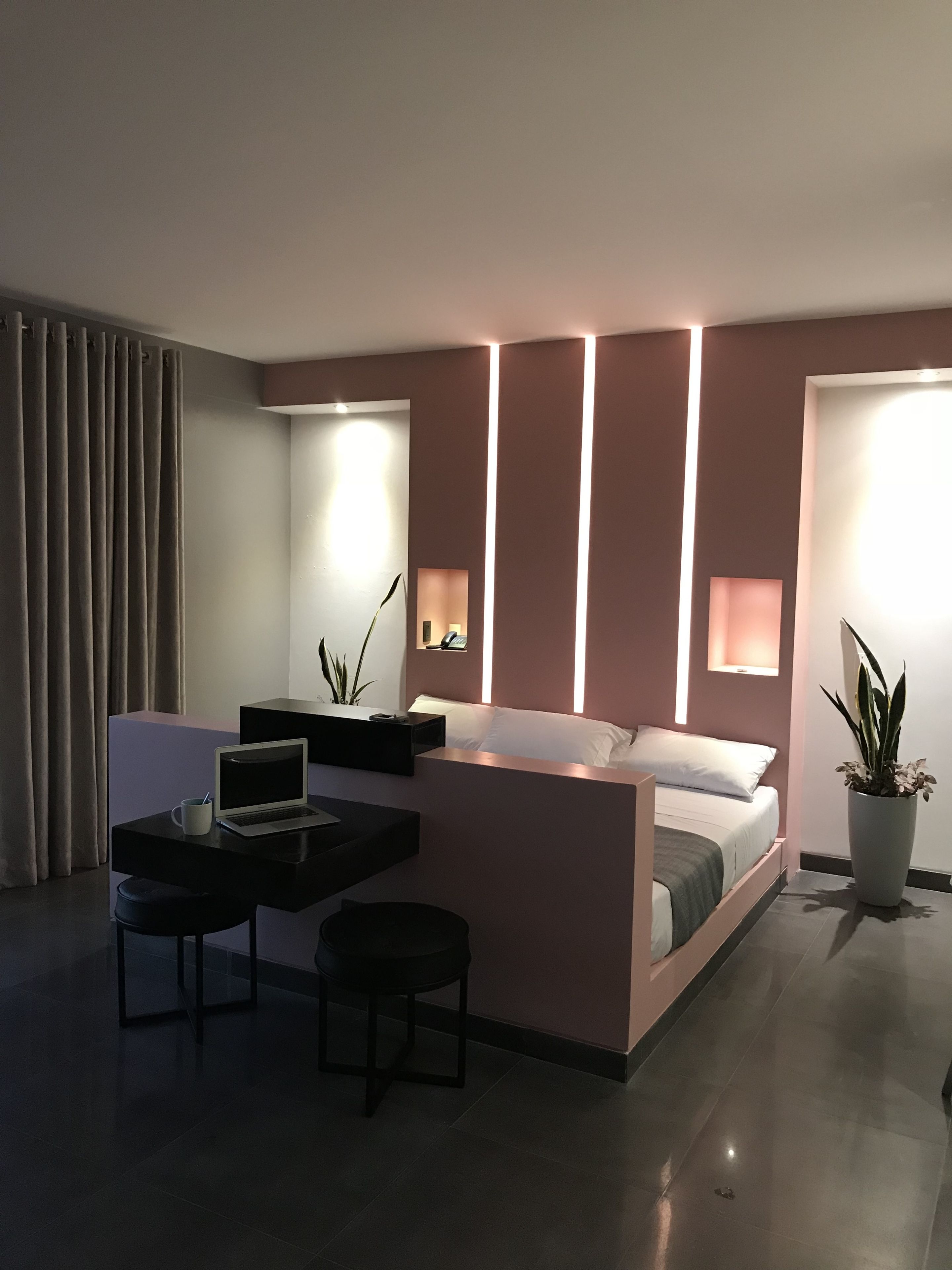 Habitación de hotel moderna con una cama, un escritorio con una computadora portátil, una silla y una planta en maceta.