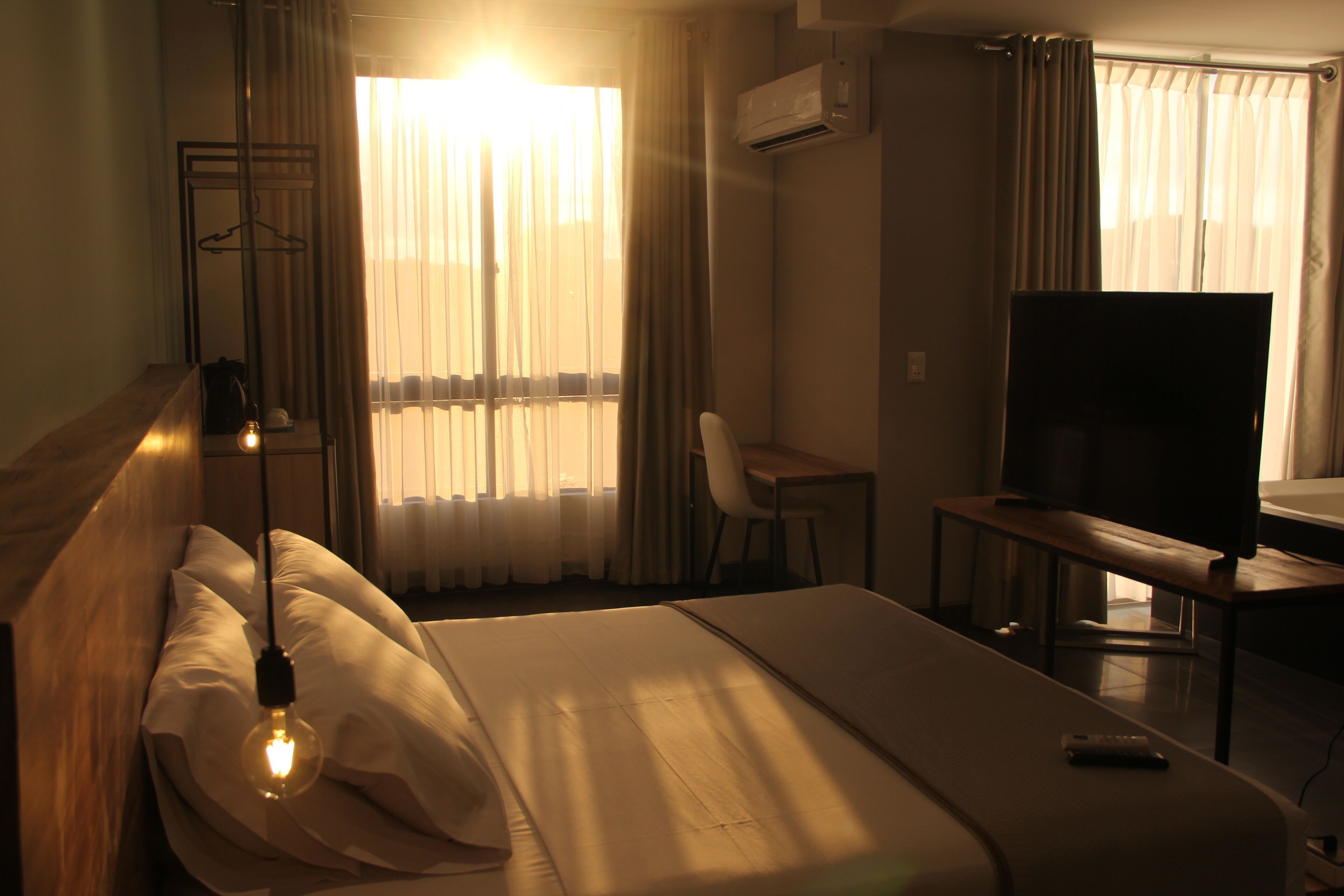 A hotel room with a bed, a desk, a television, and a window with curtains.