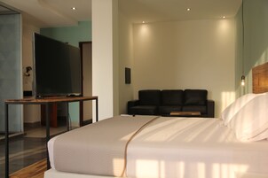 Una habitación de hotel moderna con una cama grande, un televisor sobre una mesa de madera y un sofá de color oscuro.