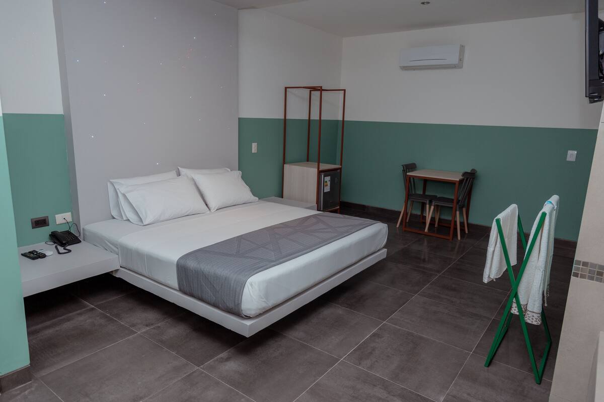 A bedroom with a bed, bedside table, chair, and a small table with a mirror.