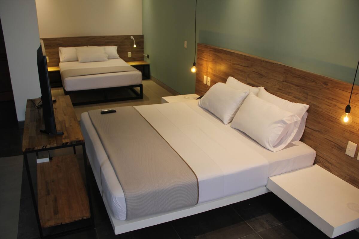A modern hotel room with a large bed, a smaller bed, a desk with a chair, and a TV.
