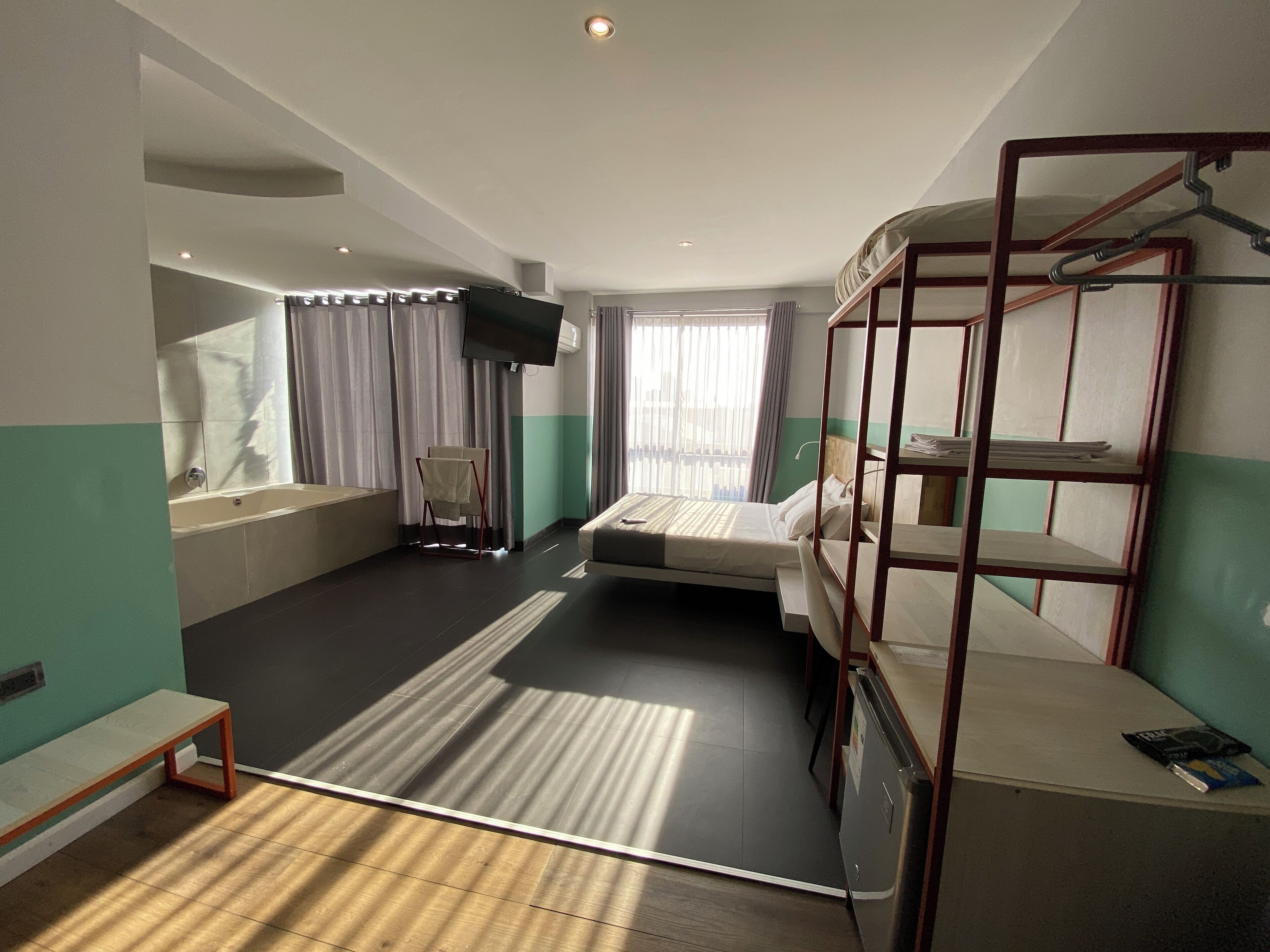 Quarto de hotel compacto com uma cama de solteiro, uma pequena escrivaninha, uma televisão e uma cama beliche.