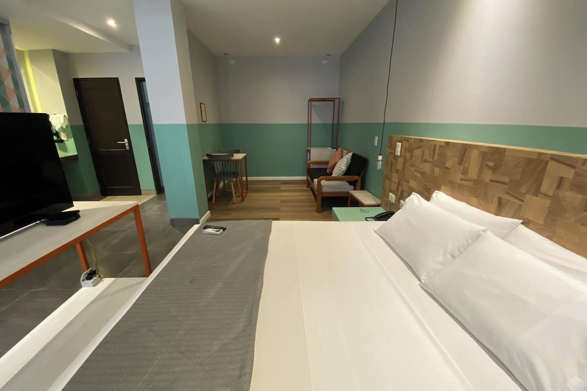 A hotel room with a bed, a desk, a chair, a TV, and a small table.