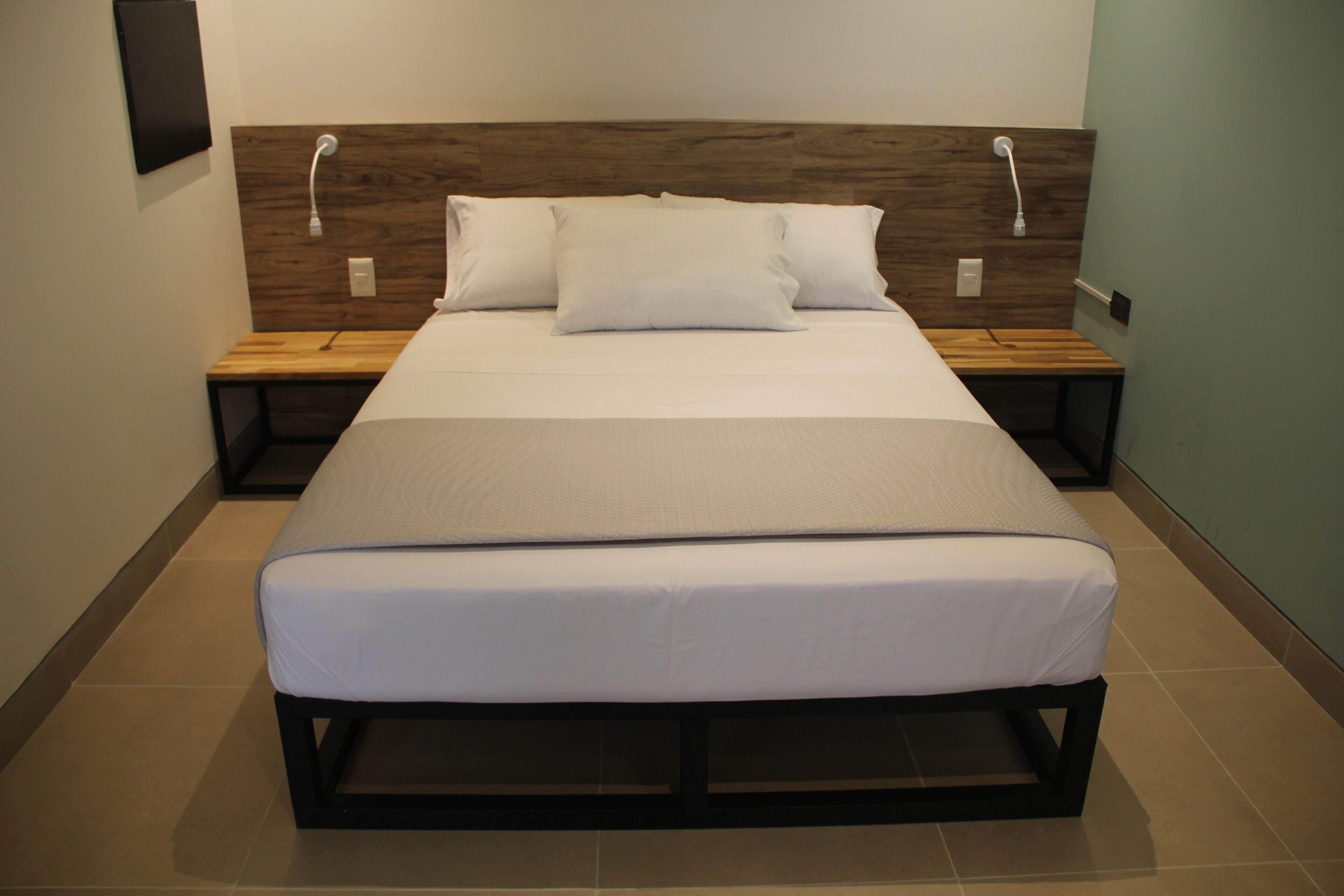 A neatly made bed with a wooden headboard, two bedside tables, and a wall-mounted light fixture.