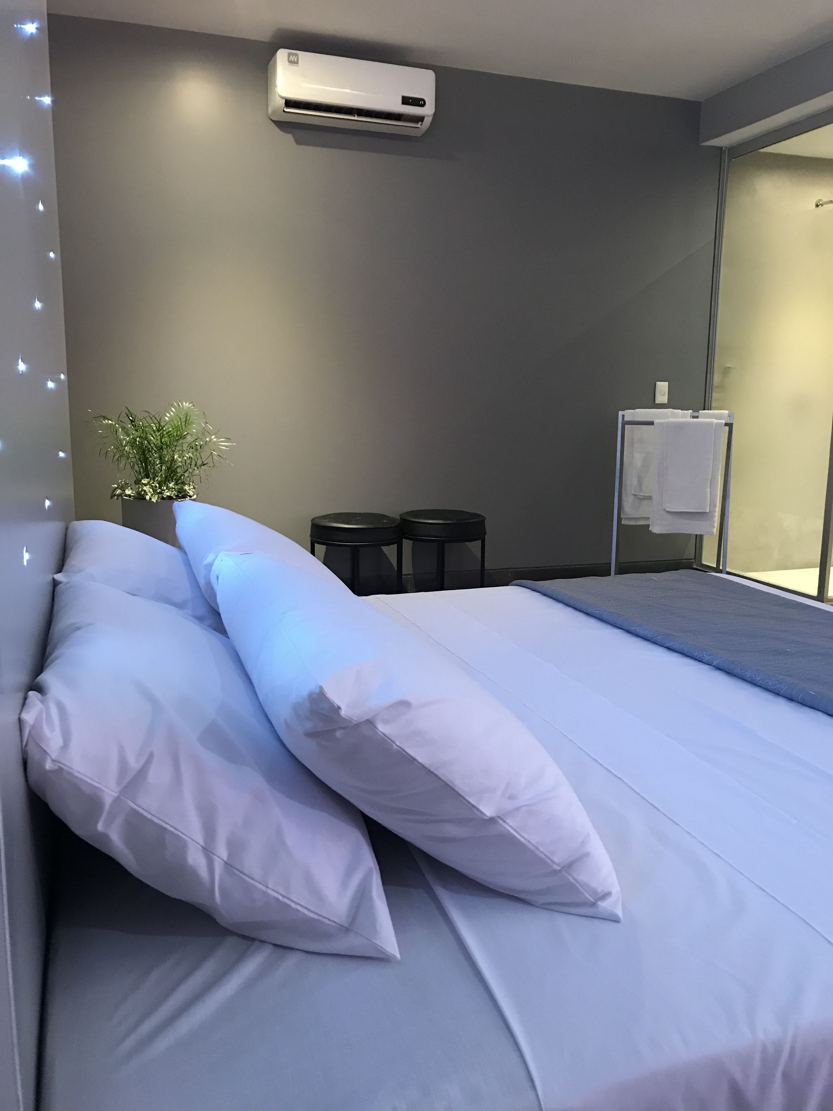Une chambre d’hôtel moderne avec un grand lit, une petite table de chevet, une plante en pot et un appareil de climatisation.