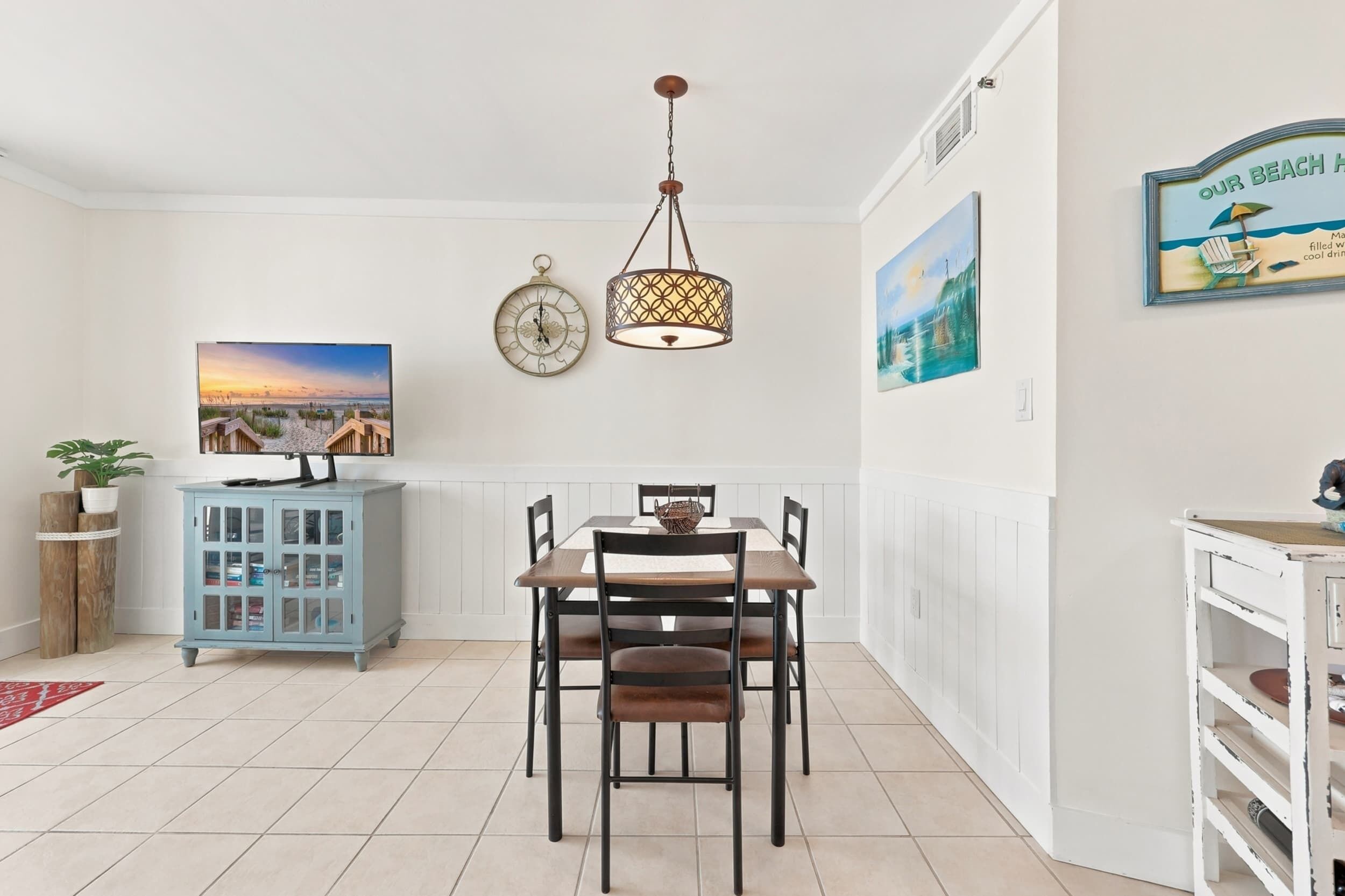 A dining area with a wooden table, chairs, a hanging light fixture, a clock, and wall art.