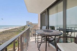 A balcony with a table and chairs, overlooking a beach and buildings. - Oceanfront in Heart of N Myrtle  Beach with Pool (North Myrtle Beach)