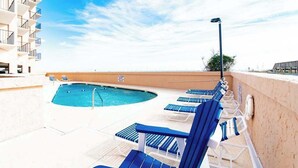 Una piscina sul tetto con comode poltrone blu, cielo sereno e un edificio con balconi.