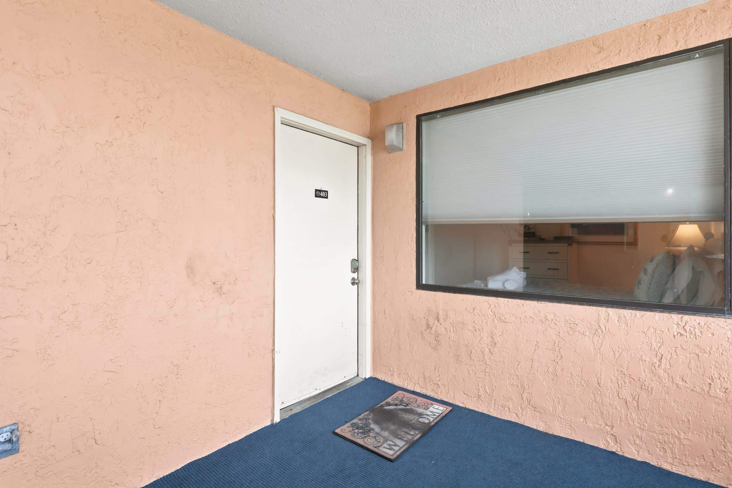 A room with a door marked 'E403,' a window with blinds, and a doormat.