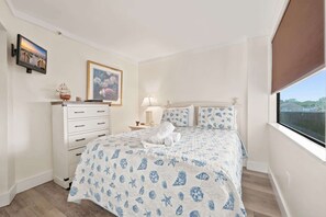 A bedroom with a bed, a dresser, a nightstand, a lamp, a framed picture, and a window. - Oceanfront in Heart of N Myrtle  Beach with Pool (North Myrtle Beach)