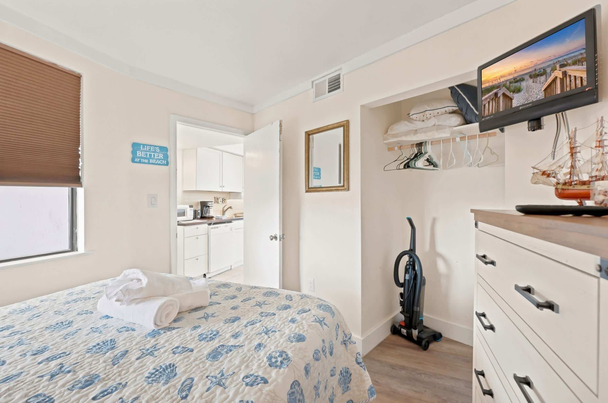 Een slaapkamer met een bed, een televisie, een spiegel, een stofzuiger en een bord aan de muur.