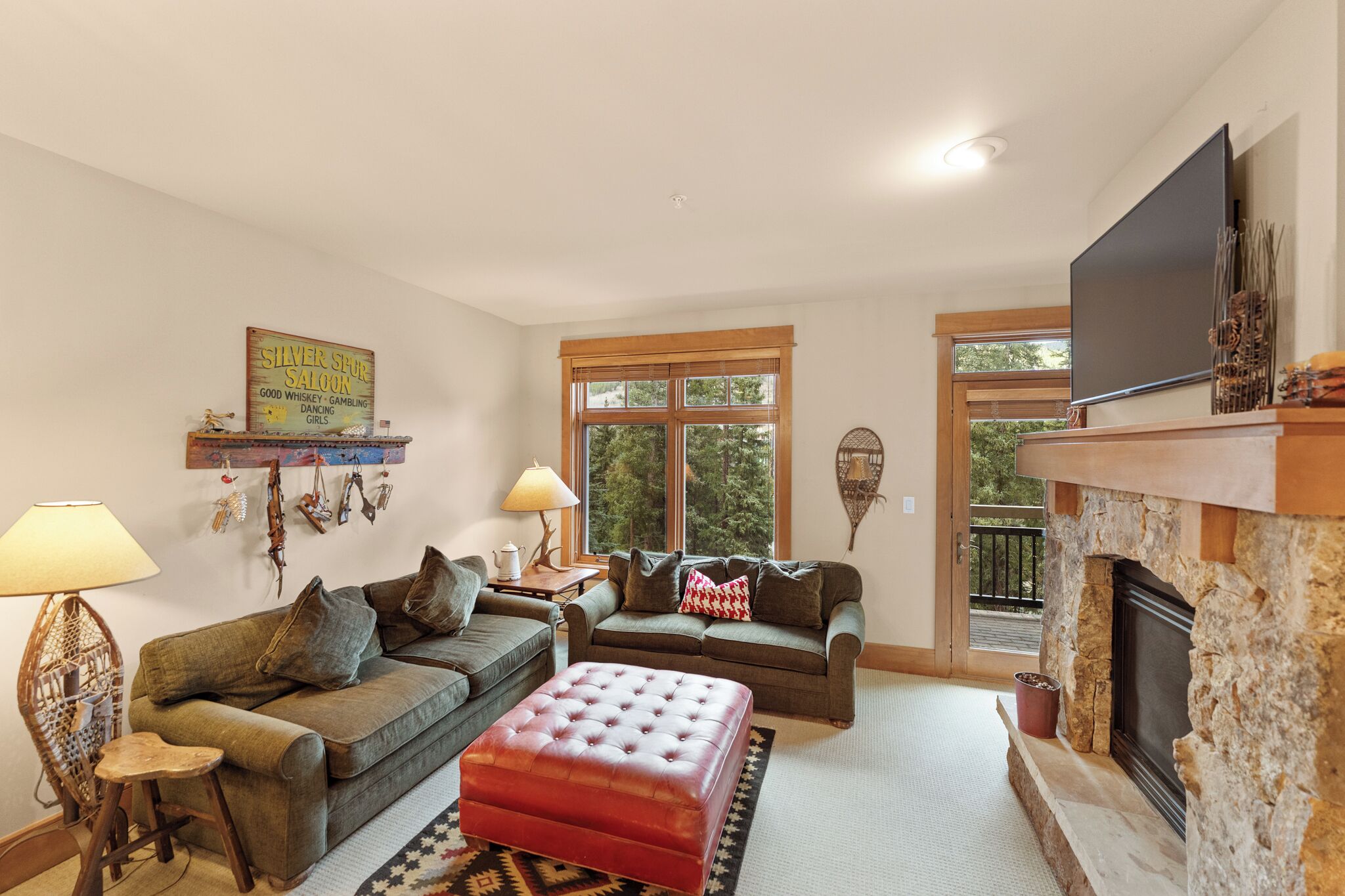 A cozy living room with two sofas, a red ottoman, a fireplace, and a television on the wall.