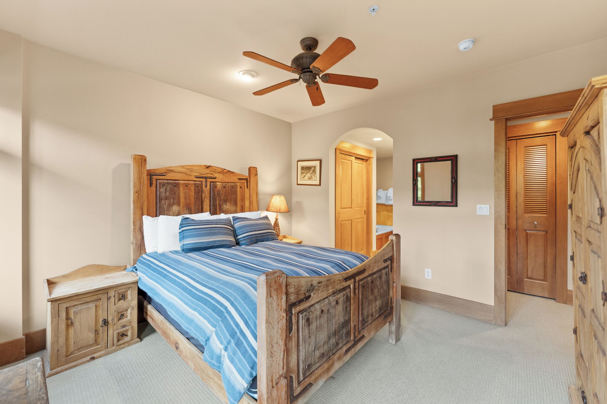 Une chambre avec un lit en bois, un ventilateur de plafond, une table de chevet et une armoire.