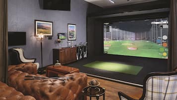 A room with a large screen displaying a golf game, leather furniture, a globe, and framed pictures on the wall.