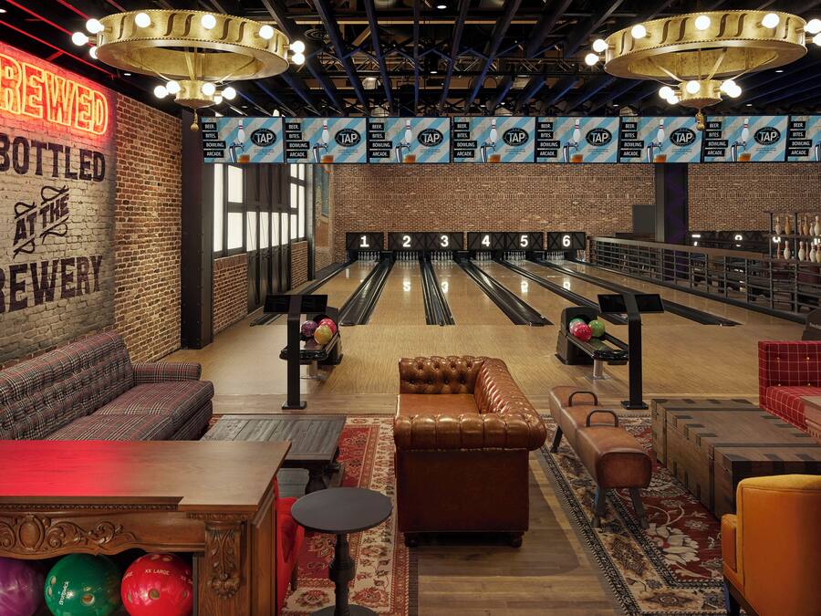 A bowling alley with a neon sign reading "BREWED & BOTTLED AT THE BREWERY" and multiple bowling lanes.