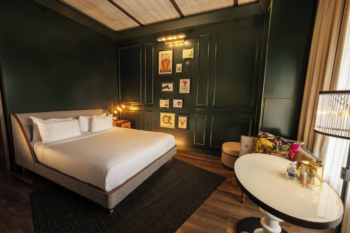 A hotel room with a large bed, a small round table, and a wall decorated with framed pictures.