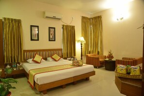 A hotel room with a large bed, a desk, a chair, a lamp, and a small table with snacks. - Pai Vista, KR Road, Bangalore (Bengaluru)