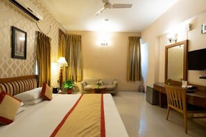 A hotel room with a bed, a desk, a chair, a sofa, a TV, and a ceiling fan.