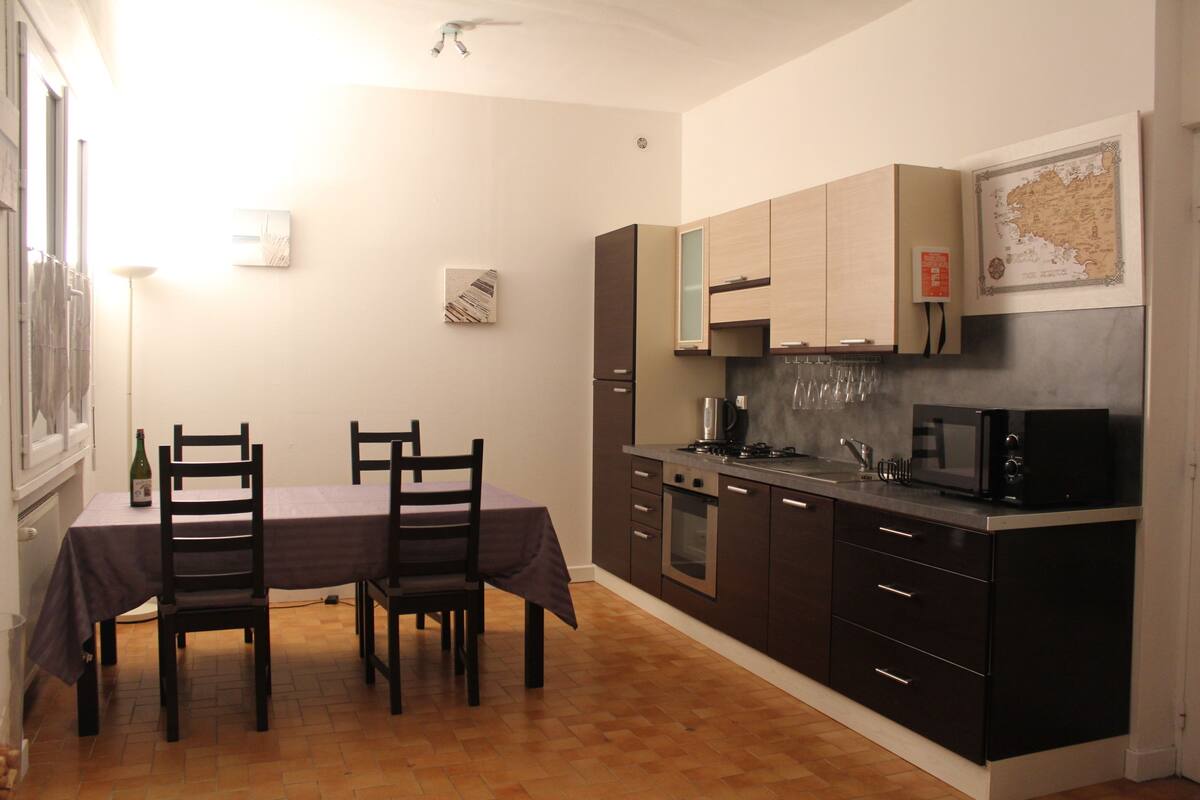 Cocina pequeña con armarios oscuros, microondas y estufa. Hay una mesa de comedor con sillas y un mapa en la pared.
