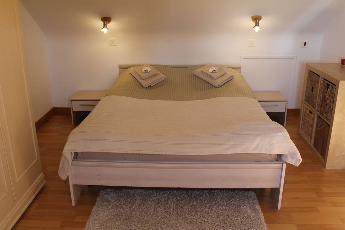 Un dormitorio con una cama, dos mesitas de noche, un aparador, un armario de madera y una alfombra.