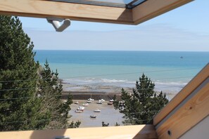 Vista dalla finestra su una spiaggia con barche, alberi e cielo sereno.