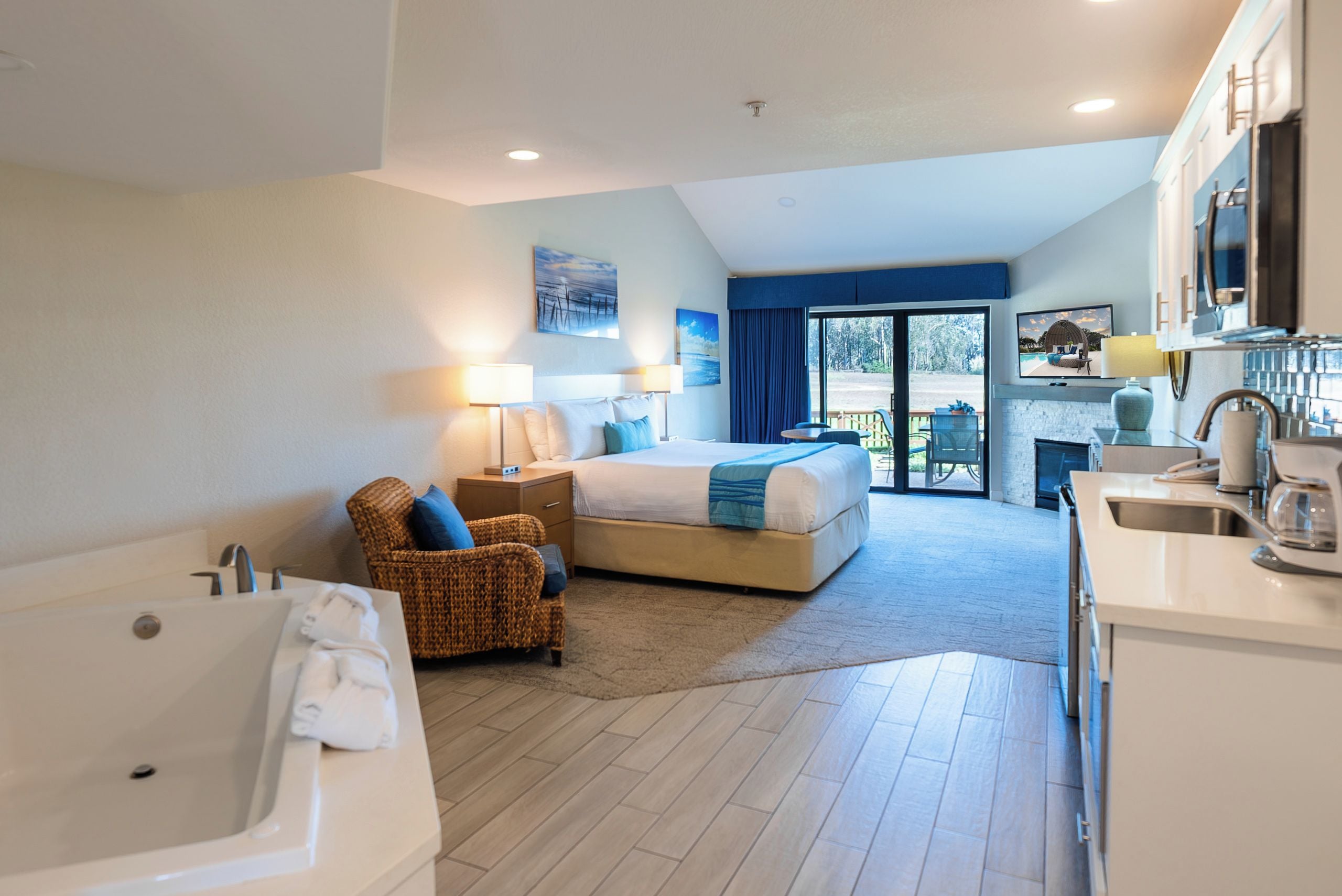 A hotel room with a bed, a sitting area with a chair, a bathtub, a television, and a view of the outdoors.