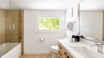 A modern bathroom with a glass-enclosed shower, a toilet, a sink with a mirror, and a window providing natural light.