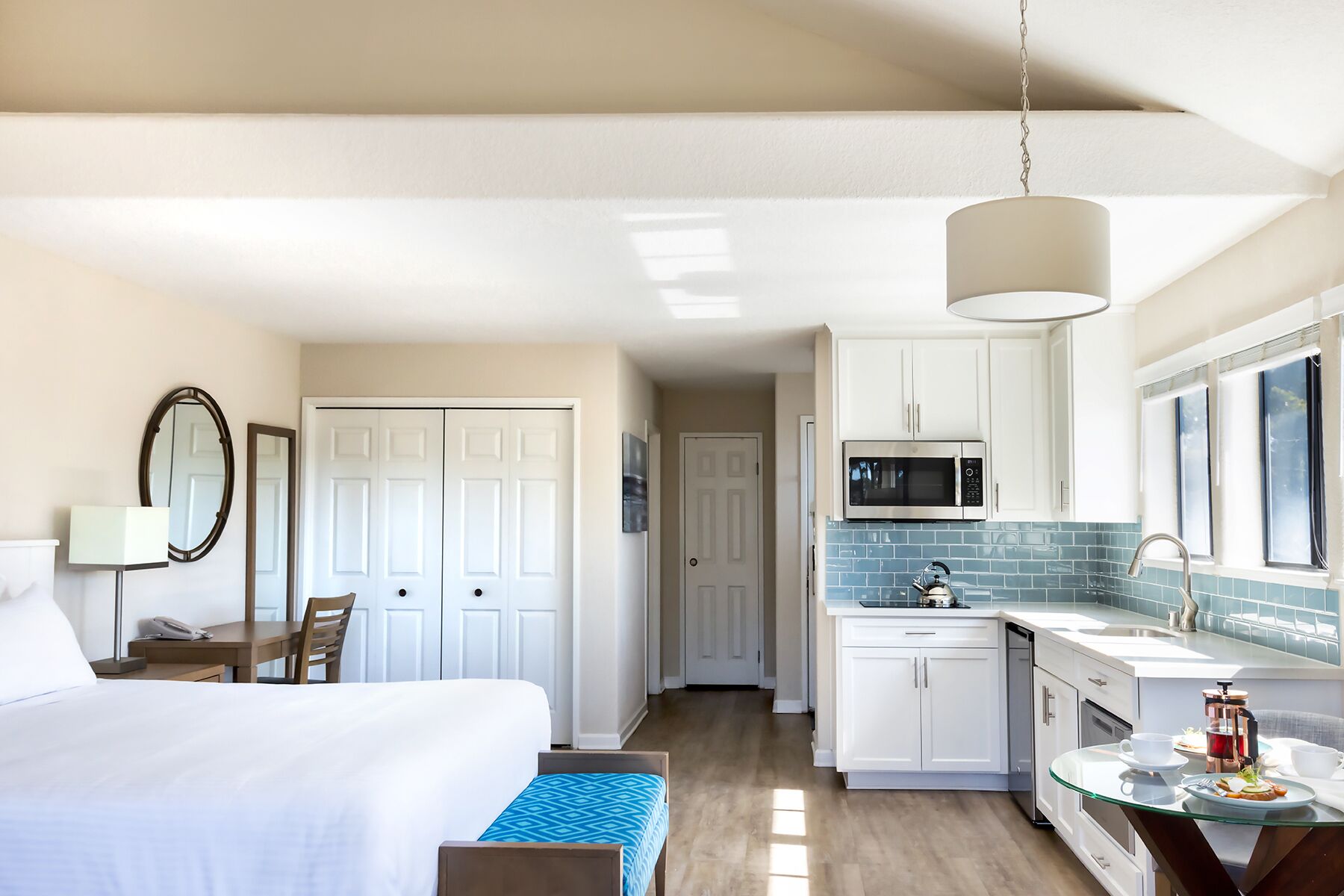 A hotel room with a bed, bedside table, lamp, and a view of the kitchen area.
